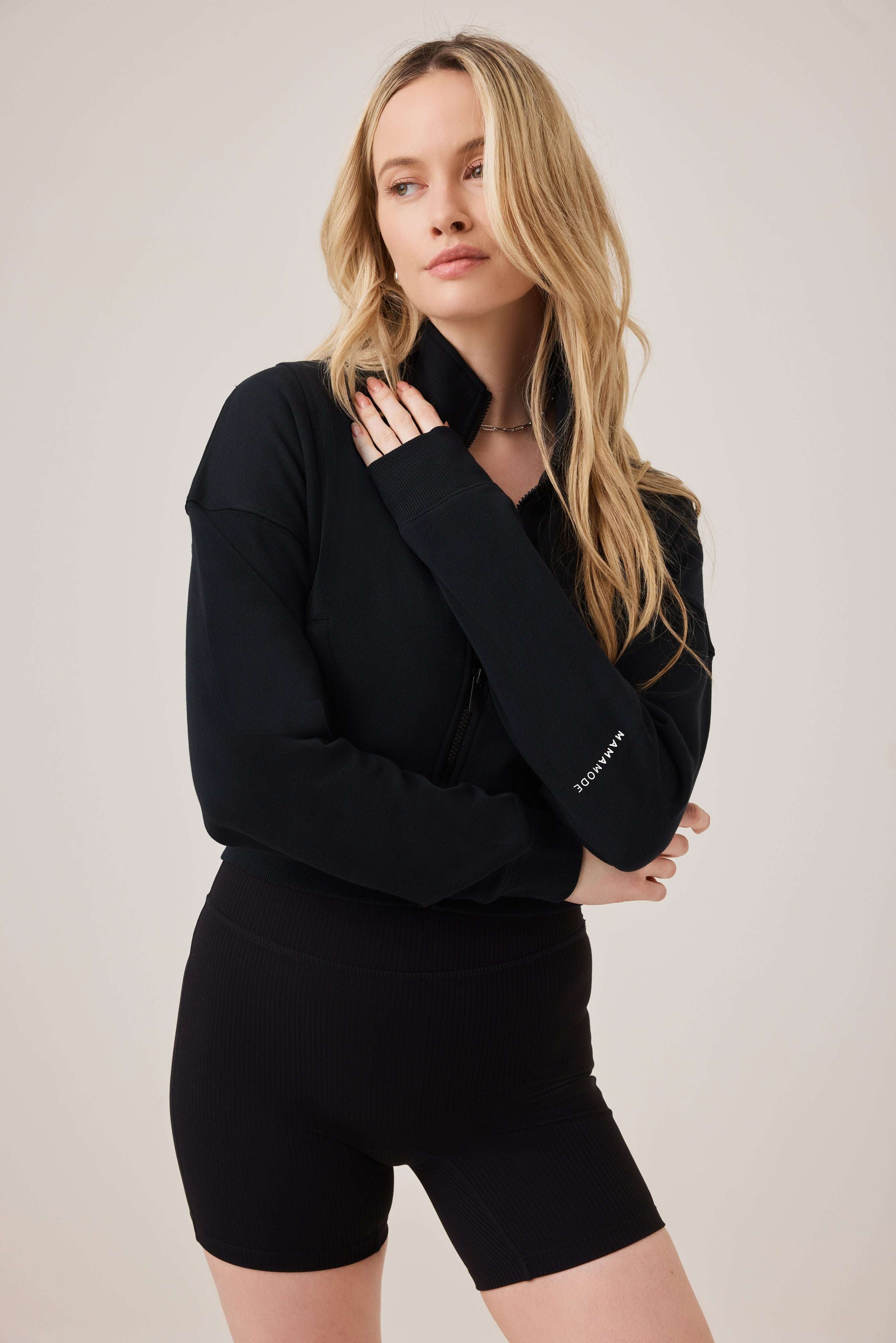 Woman wearing a black outfit with a brand logo on a plain background