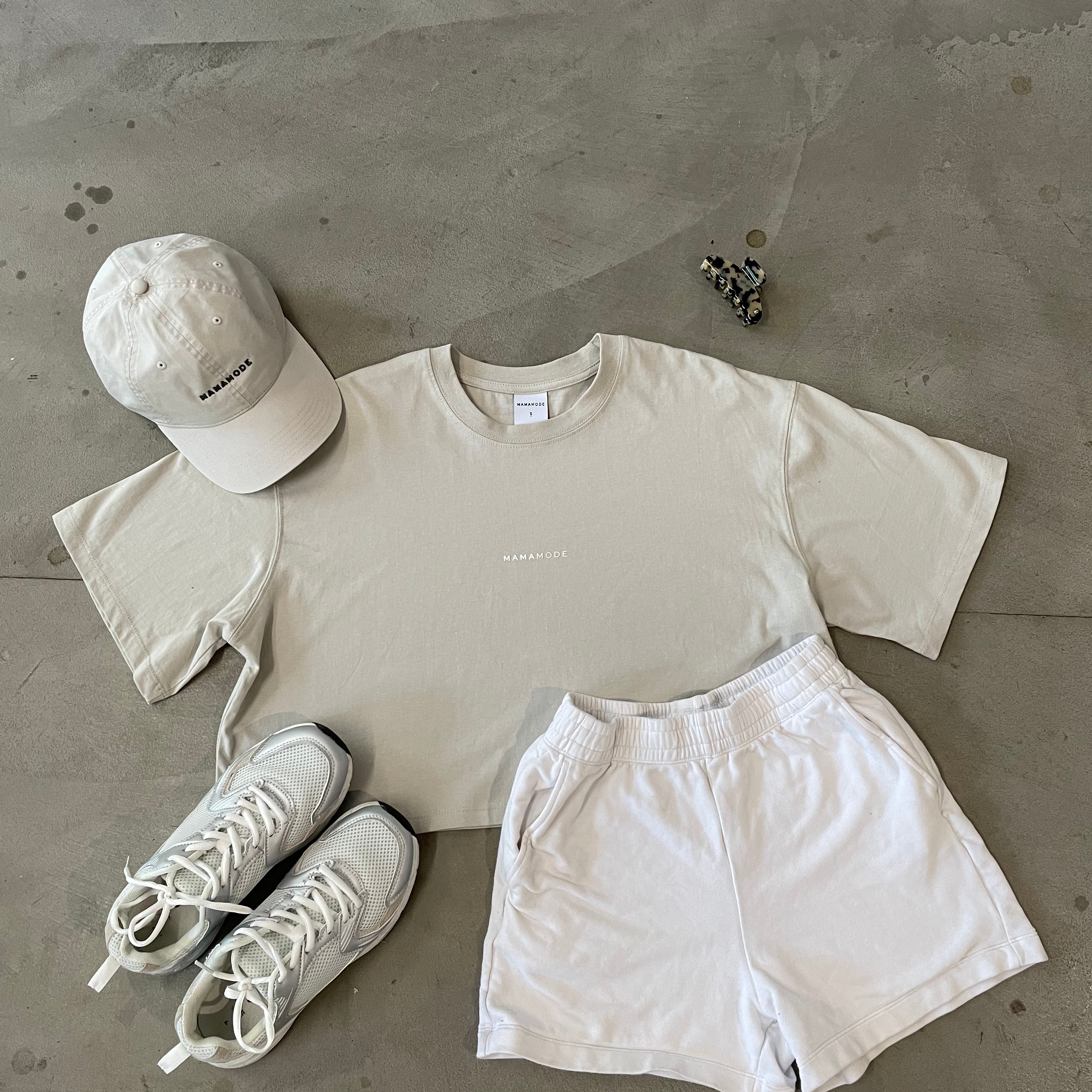 Light-colored t-shirt, shorts, cap, and sneakers arranged on a concrete surface.
